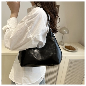 Detail of black glossy crescent bag with fashion embossing on shoulder of model