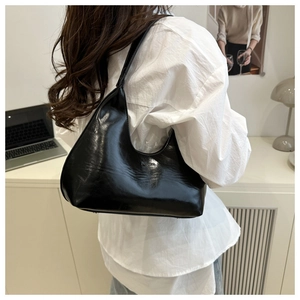 Detail of glossy black faux leather crescent bag with embossed logo on shoulder strap