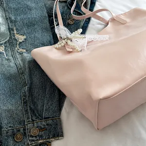 Detail van lichtroze tote tas met kanten strik en parelhanger op glad kunstleer