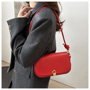 Close-up of bright red shoulder bag featuring gold circular buckle and knot strap detail