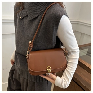 Close-up of caramel brown leather shoulder bag with decorative gold circular buckle and knot