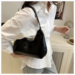 Close-up of a minimalist black glossy underarm crescent bag worn with a white shirt