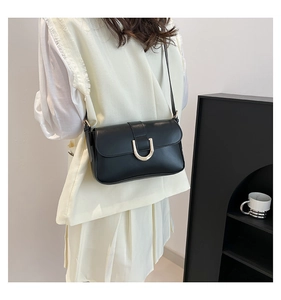 Detailansicht einer schwarzen Leder-Baguette-Tasche mit goldener Hufeisenschnalle am Model