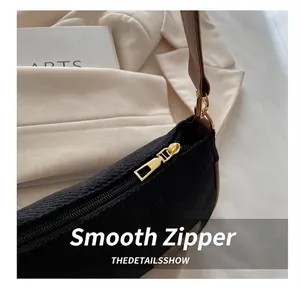 Detail of smooth gold zipper and black textured fabric on a minimalist shoulder bag