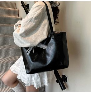 Detail of black glossy tote bag featuring white lace and pearl bow accent on the side