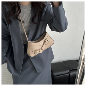 Détail d'un sac sous le bras beige avec boucles dorées associé à un blazer bleu clair