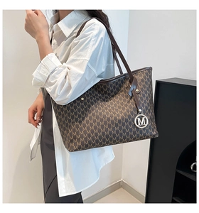 Detalle de un bolso tote grande marrón con monograma, colgante M dorado y correas finas