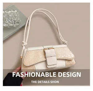 Detail of white crocodile-embossed underarm bag with decorative buckle and knotted strap