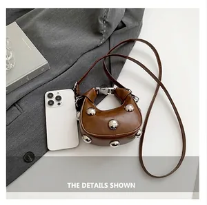 Micro brown crossbody bag with silver rivets compared to a smartphone for scale