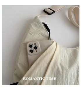 Détail d'un sac dumpling en nylon beige avec une poche latérale pour un smartphone