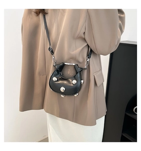 Detail of black mini crossbody bag with silver rivet studs worn by a model