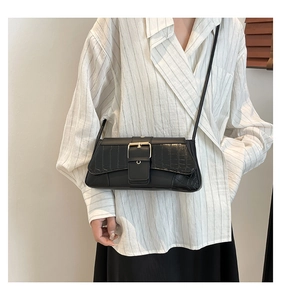 Detail of black crocodile texture shoulder bag with gold buckle on a model outfit