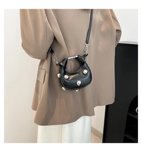 Detail of mini black crescent bag featuring silver rivet accents and crossbody strap