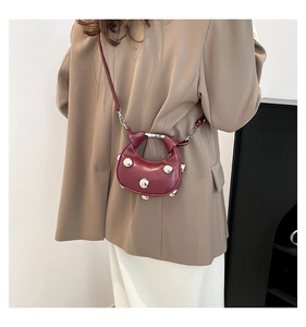 Close-up of a burgundy leather half-moon bag with large silver stud accents and metallic hardware