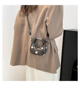 Close-up of matte dark coffee leather crescent bag with bold silver metal rivet studs