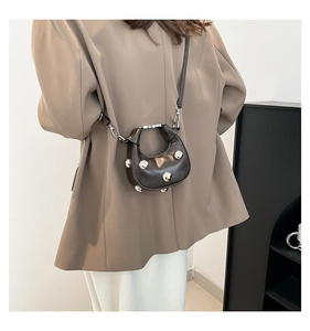 Close-up of semi-circle crossbody bag with silver studs on a dark brown surface