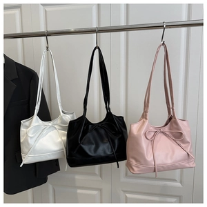 Detailed view of white, black, and pink tote bags with bow decoration hanging on a rack