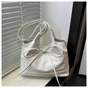 Close-up of white leather tote bag featuring a long bow detail and fine stitching texture