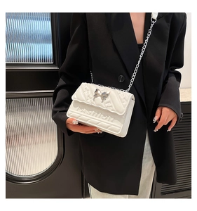Detailed view of a white quilted shoulder bag with a silver butterfly clasp and chain