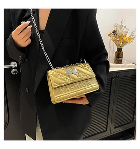 Detail of gold metallic crossbody bag with diamond quilting and silver butterfly charm