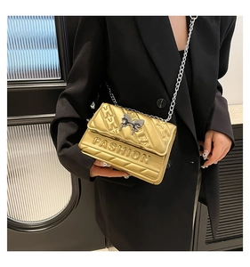 Detail of gold quilted crossbody bag with butterfly buckle and chain strap on model