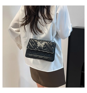 Detail of black quilted chain bag featuring a silver butterfly buckle and FASHION emboss