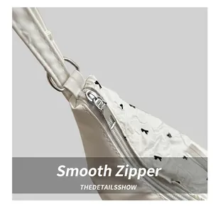 Close-up of smooth silver zipper and black bow embroidery on white PU leather bag