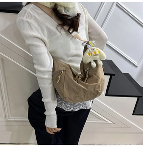 Detailed view of the brown crescent bag with adjustable wide strap and plush pendant