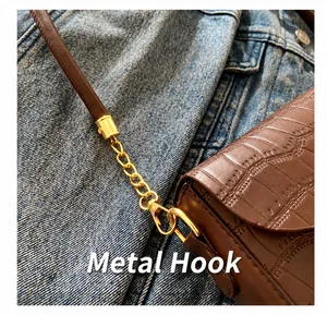 Close-up of golden metal hook and crocodile texture on a brown leather shoulder bag