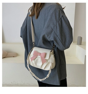 Détail du sac plissé blanc avec nœud rose et poignée tressée porté par un modèle