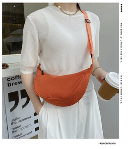 Detail of a bright orange nylon half-moon crossbody bag with adjustable strap and zipper