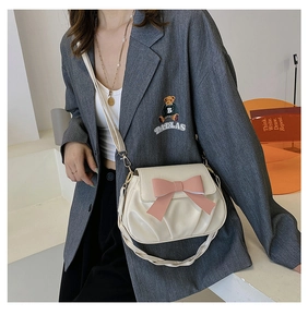 Détail du sac bandoulière crème avec un nœud rose et une finition en similicuir plissé