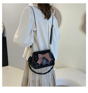 Detail van zwarte crossbodytas met contrasterende bruine strik en gevlochten handvat