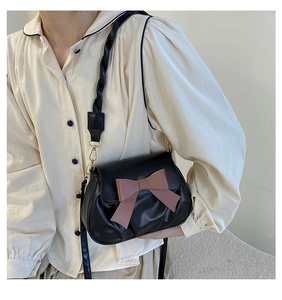 Detail van zwarte crossbody tas met roze strik en geweven riem op beige shirt