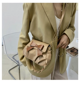 Detail van geplooide beige crossbodytas met bruine strik en goudkleurige metalen haakjes