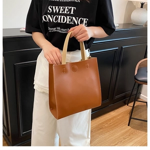 Close-up of minimalist brown leather tote bag with cream handles in a home setting