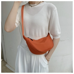 Detailed view of orange nylon crescent bag worn crossbody against a white outfit