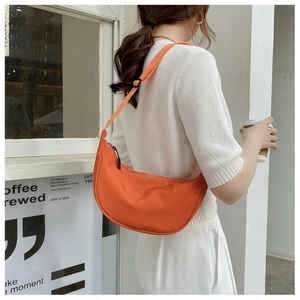 Minimalist orange crescent crossbody nylon bag worn with a white casual outfit