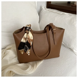 Detail of caramel leather tote bag handle decorated with an elegant patterned silk scarf