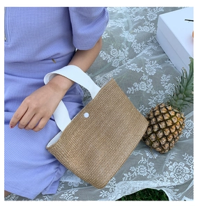 Close-up of woven straw handbag with white canvas handles and snap button detail