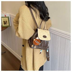 Detail van een retro mini-rugzak in bruin en beige met een schattige pluchen monsterhanger