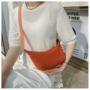 Detail view of a bright orange nylon crescent crossbody bag worn over a white outfit