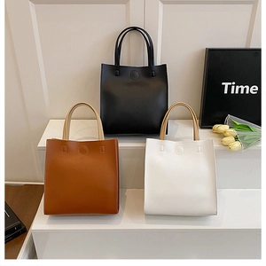 Three minimalist tote bags in black, brown and white displayed on a modern staircase