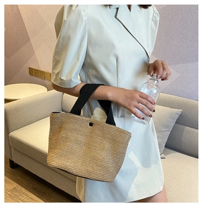 Detail of woven straw tote bag with black wide fabric handles and button closure