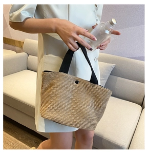 Close-up of handmade straw tote bag with black handles and button closure detail