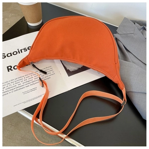 Detail of an orange crescent nylon bag with adjustable strap over a lifestyle magazine