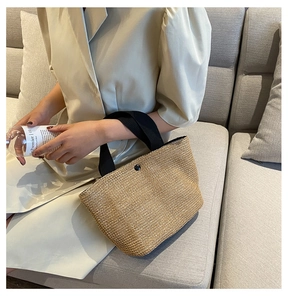 Close-up of woven straw handbag with durable black ribbon handles and metal snap closure