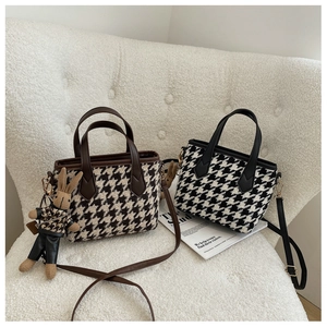 Detail of two houndstooth crossbody bags with plush bunny charm on a cozy armchair