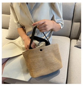 Detail of woven straw tote bag featuring black ribbon handles and decorative button