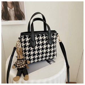 Detail of houndstooth handbag featuring a cute bunny charm and adjustable black shoulder strap